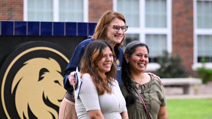 A university administrator posing with two people on a college campus.