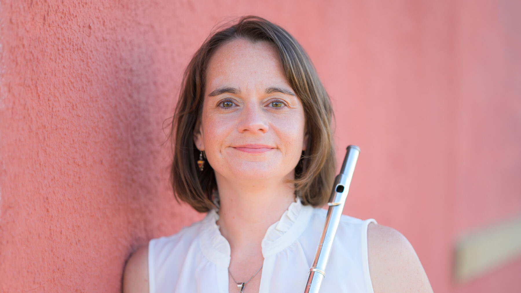 A headshot photo of a person leaning against a wall while holding a flute.
