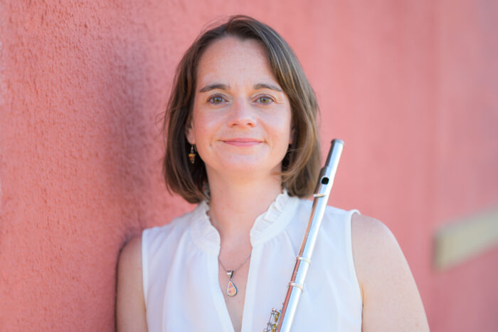 A headshot photo of a person leaning against a wall while holding a flute.