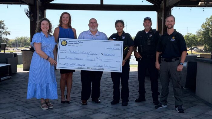 Several people standing outside holding a big check.