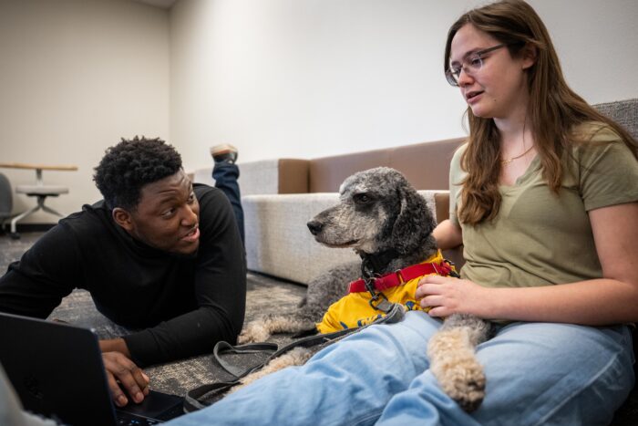 Two students sit on the floor with a service dog