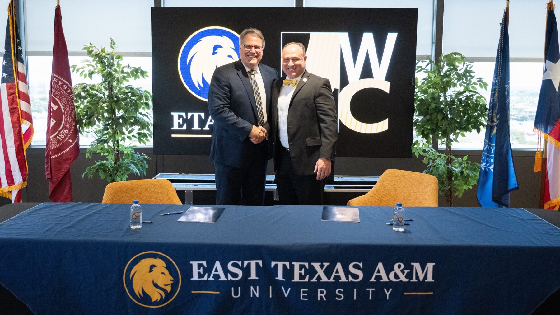 Two people in business attire shake hands after signing important documents.
