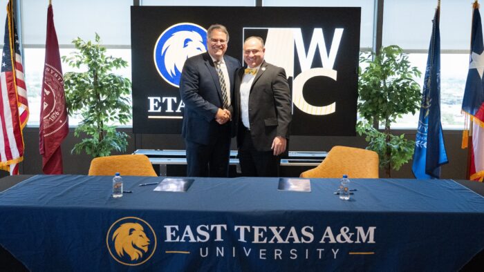 Two people in business attire shake hands after signing important documents.