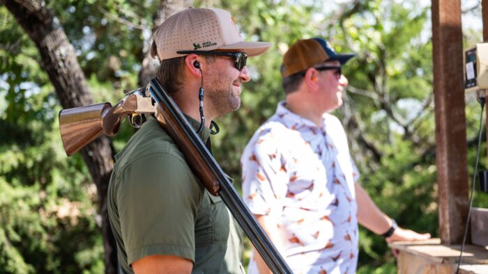 Man stands with double barrel shotgun over shoulder.