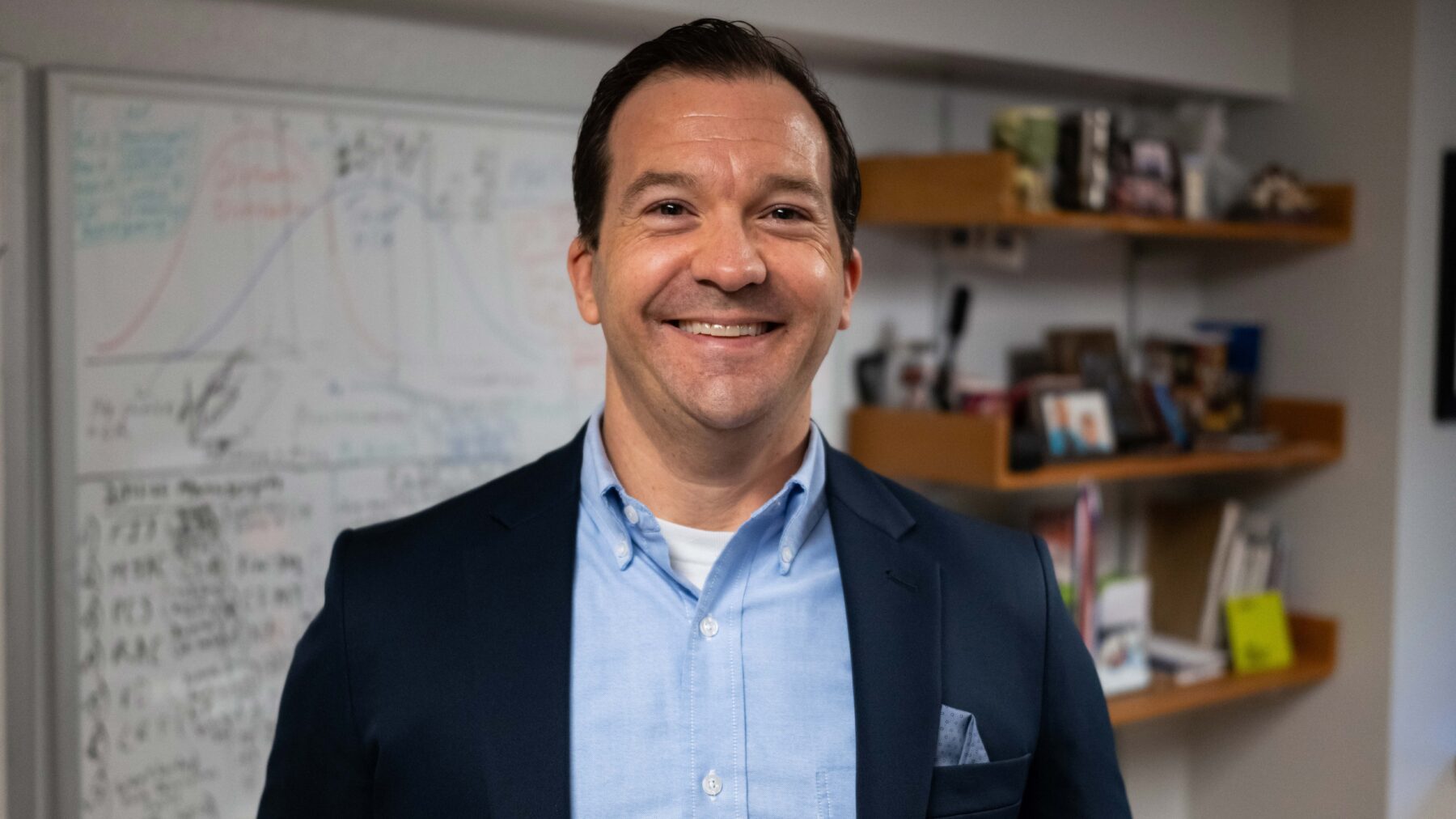 A man standing in a classroom, smiling.