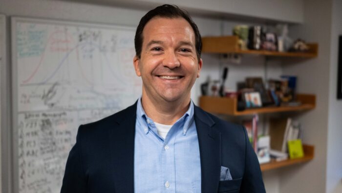 A man standing in a classroom, smiling.