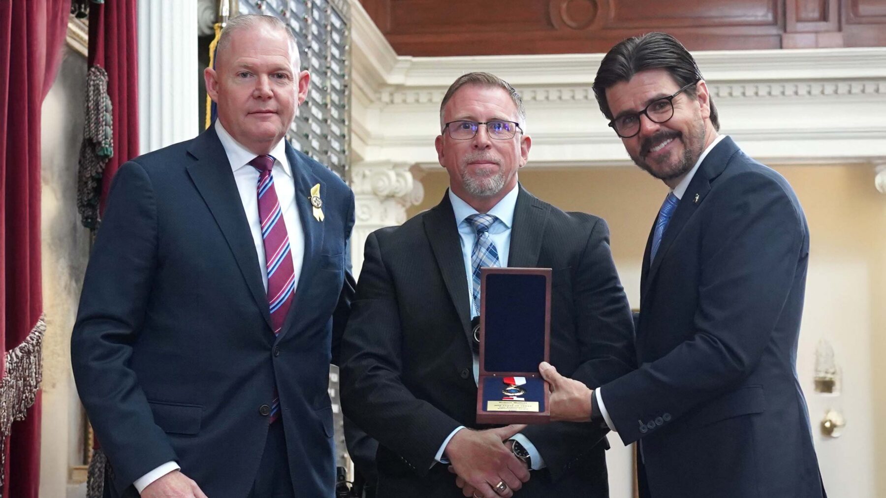 Three men stand in a row, presenting an award.