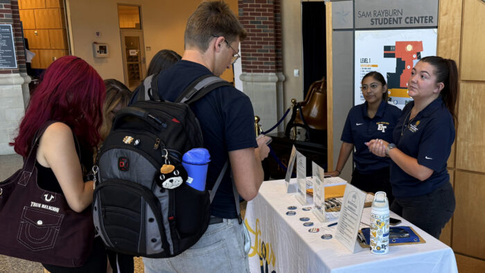 People conversing at an informational booth on a college campus.