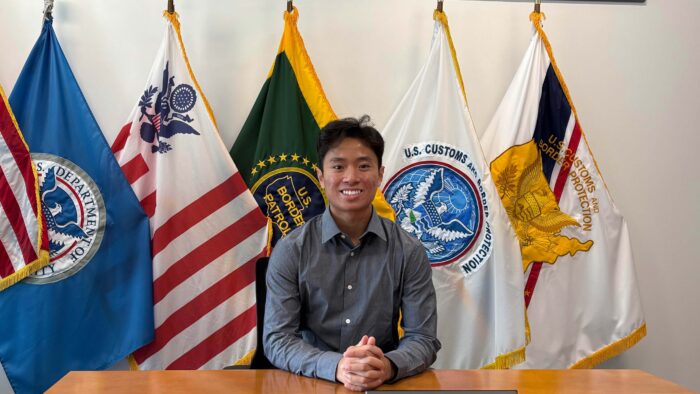 Man sitting at desk with flags behind him.