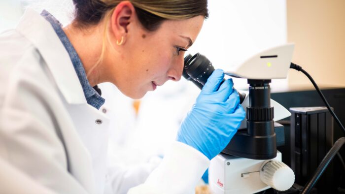 A woman looks into a microscope.