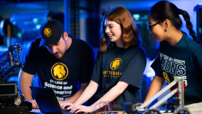 Three young people work at a lab desk with a laptop.