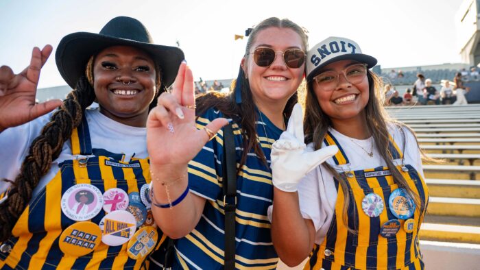 Three women make the Lion Pride symbol and smile.