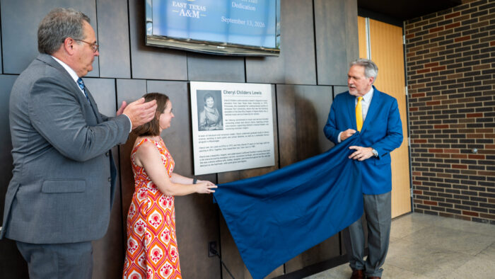 Three people unveil a plaque outside of a concert hall.