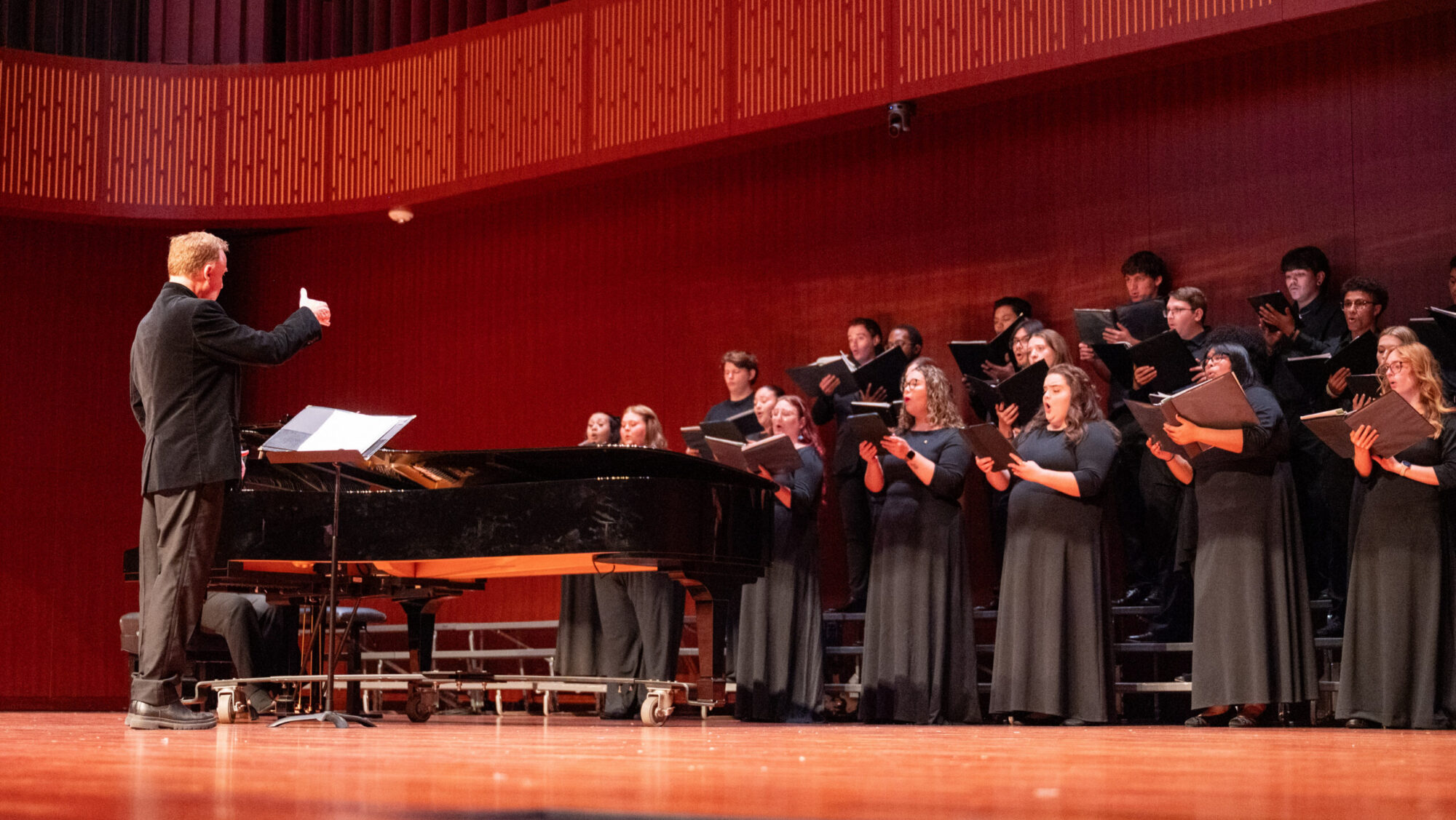 A choir director conducting a choir during a performance onstage.