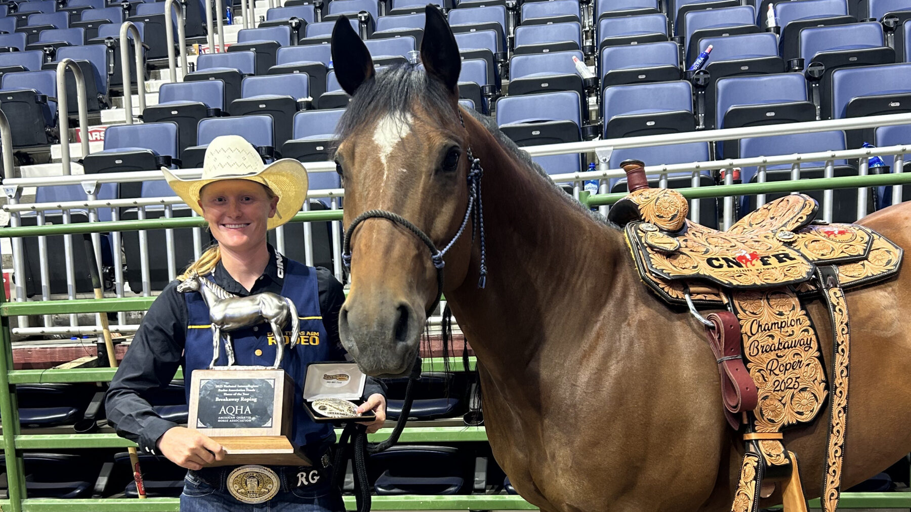 A person in western attire posing with a trophy next to a horse.