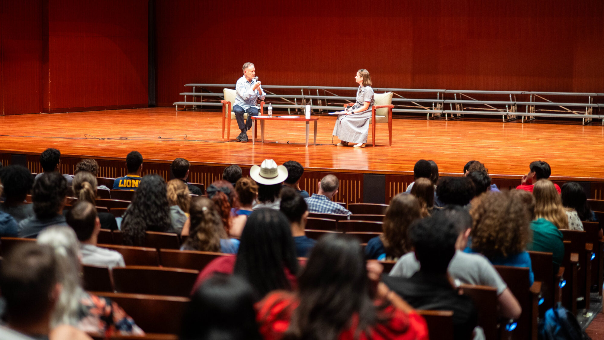 Two people speaking on a stage in front of a crowd of people.
