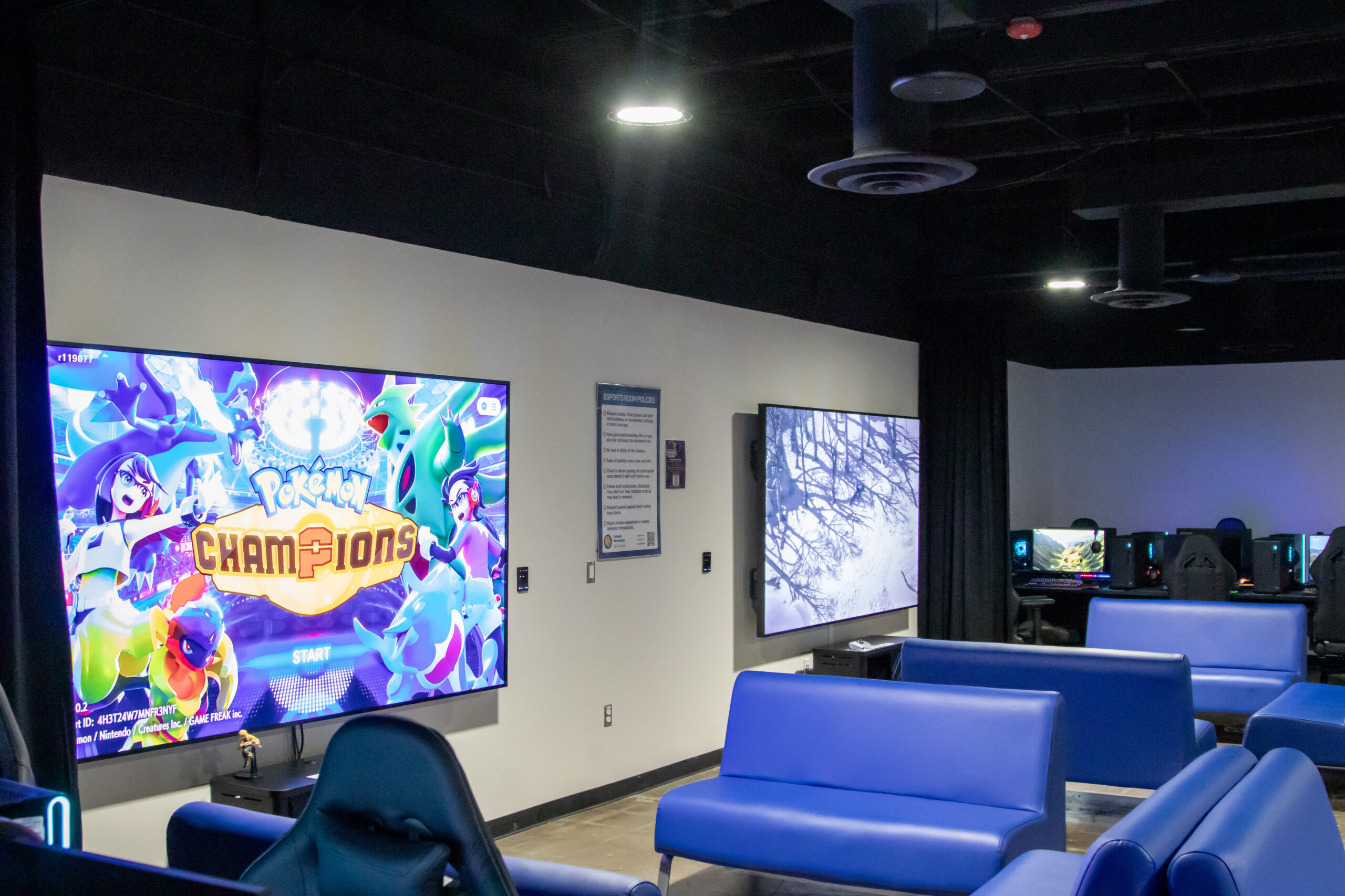 A room with two large wall-mounted TVs displaying video games.
