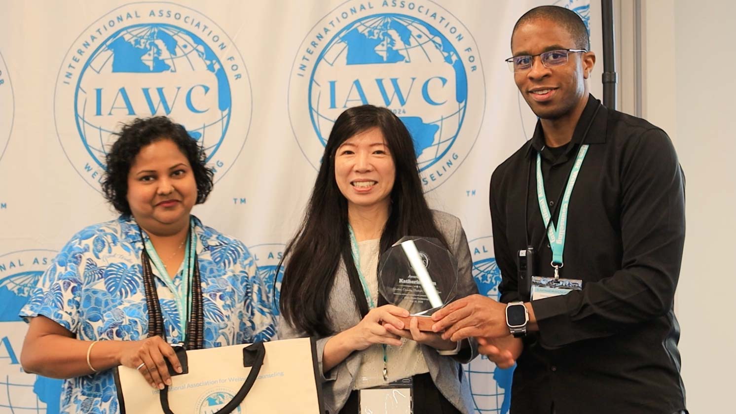 Three people stand in a row, with the center person holding a trophy.