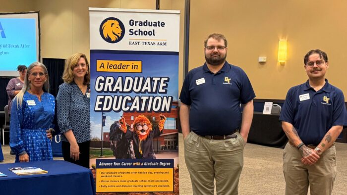 Four people stand in a row smiling, with a Graduate School sign in the middle.