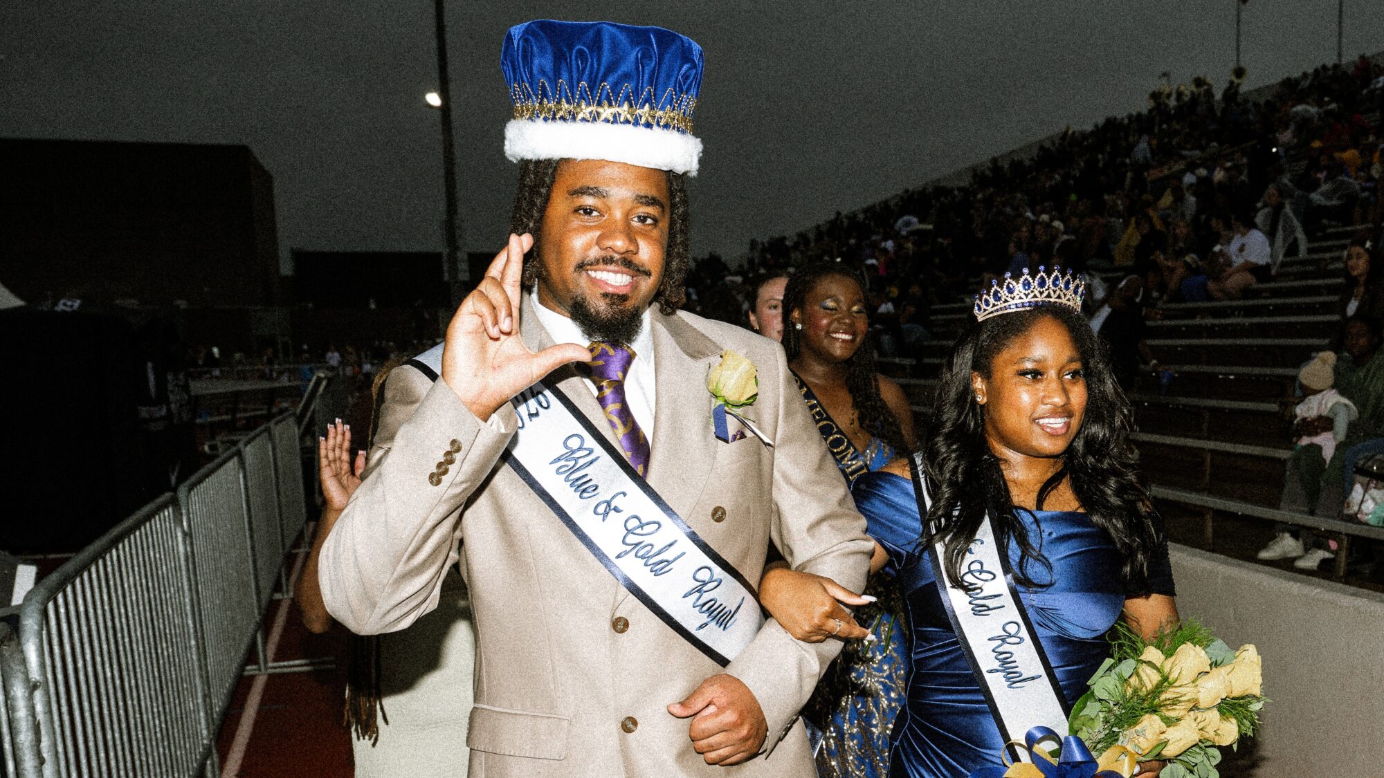 Two people in formal attire walk near the stands of a college football stadium.