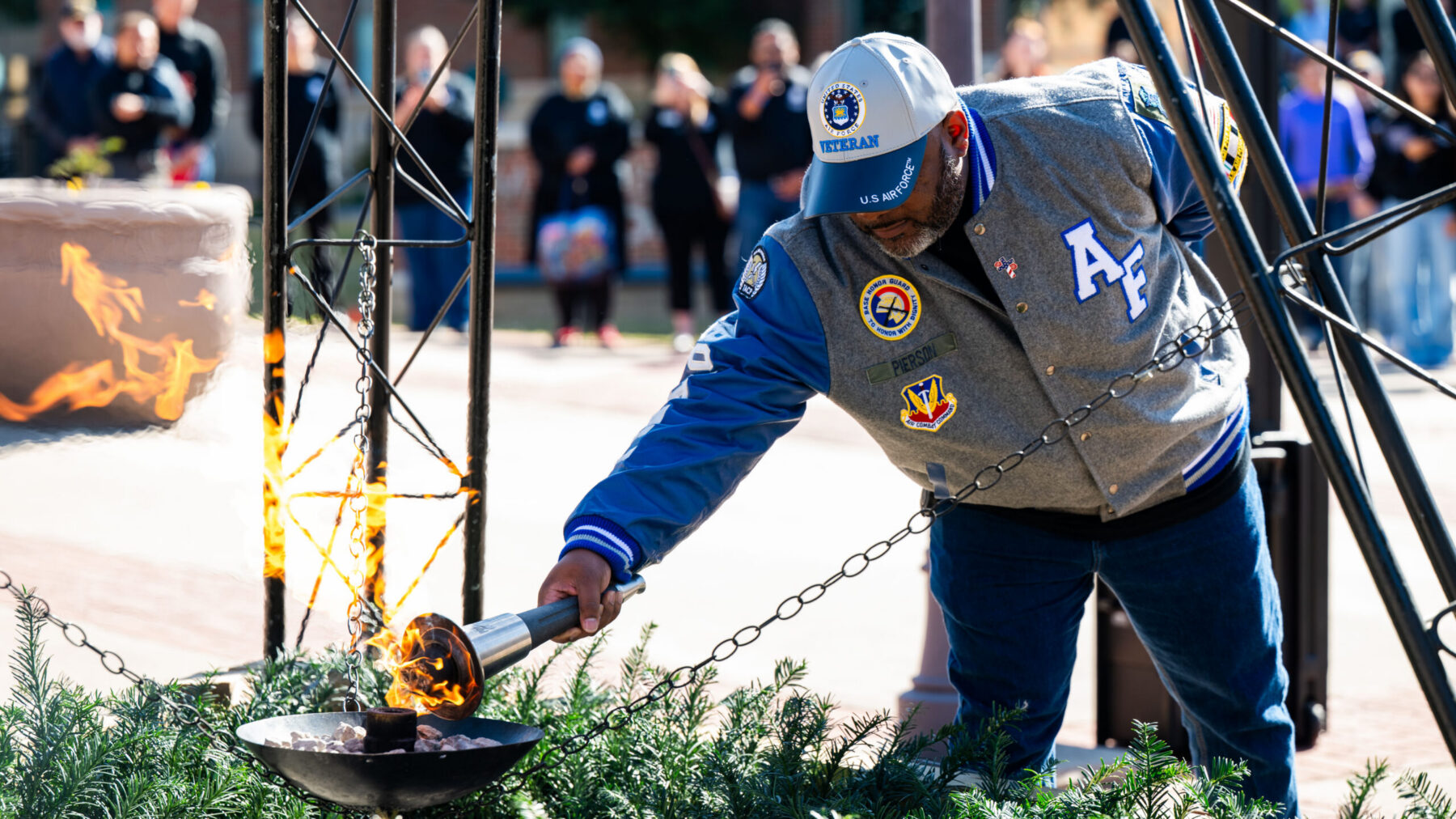 A person in a letterman jacket adorned with U.S. air force regalia uses a gas torch to light a flame.