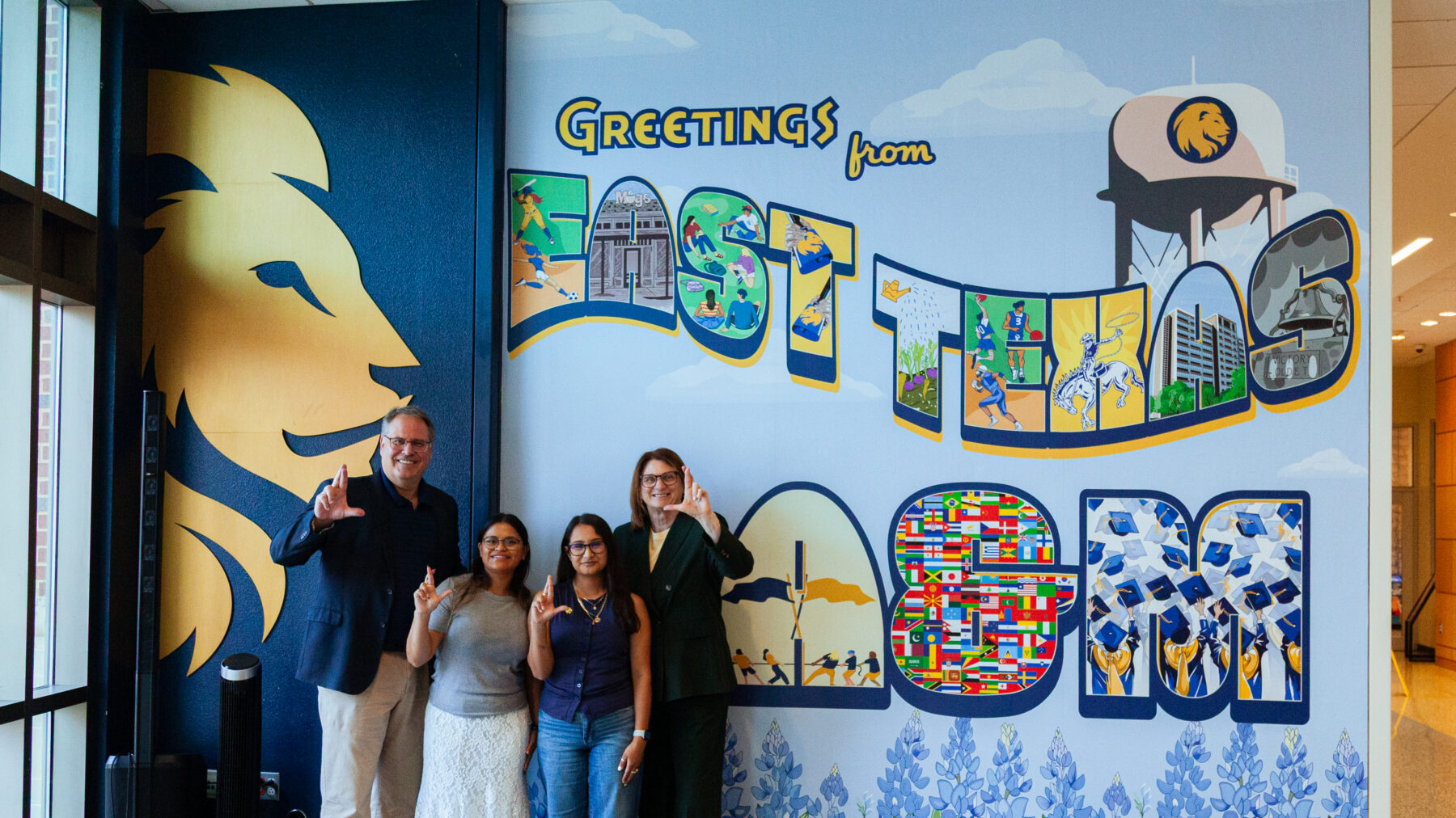 A group of people holding up the lion hand signal in front of the new mural.