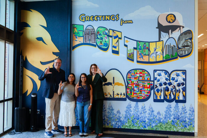 A group of people holding up the lion hand signal in front of the new mural.